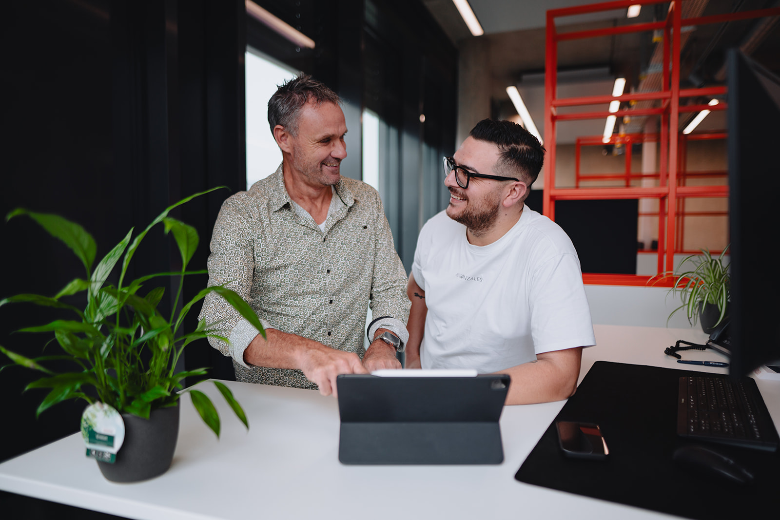 Zwei Angestellte von Braun in einer modernen Büroumgebung blicken zusammen auf ein Tablet und unterhalten sich.