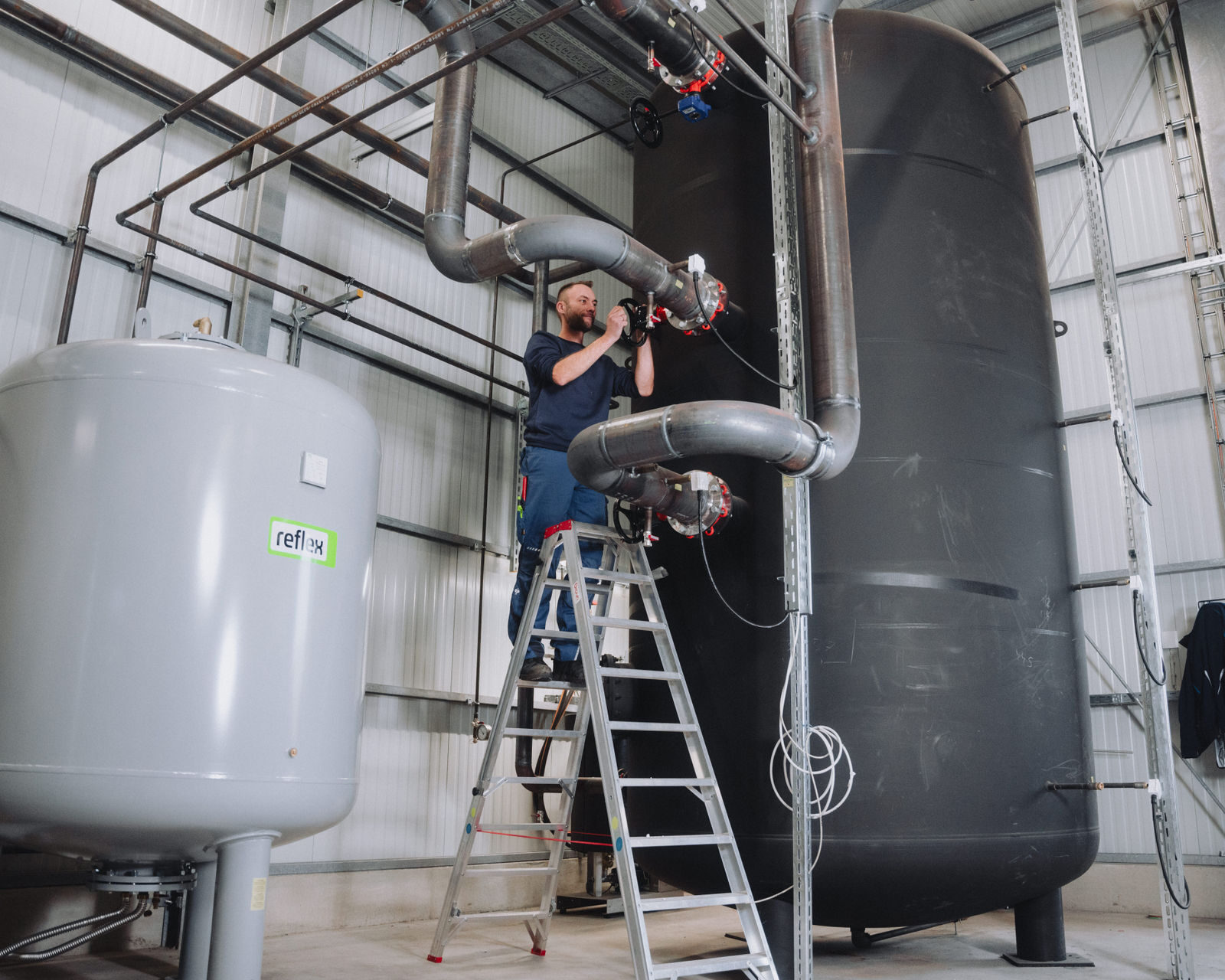 Ein Mitarbeiter von Braun betätigt auf einer Leiter stehend eine Armatur, während im Hintergrund ein großer Pufferspeicher zu sehen ist.