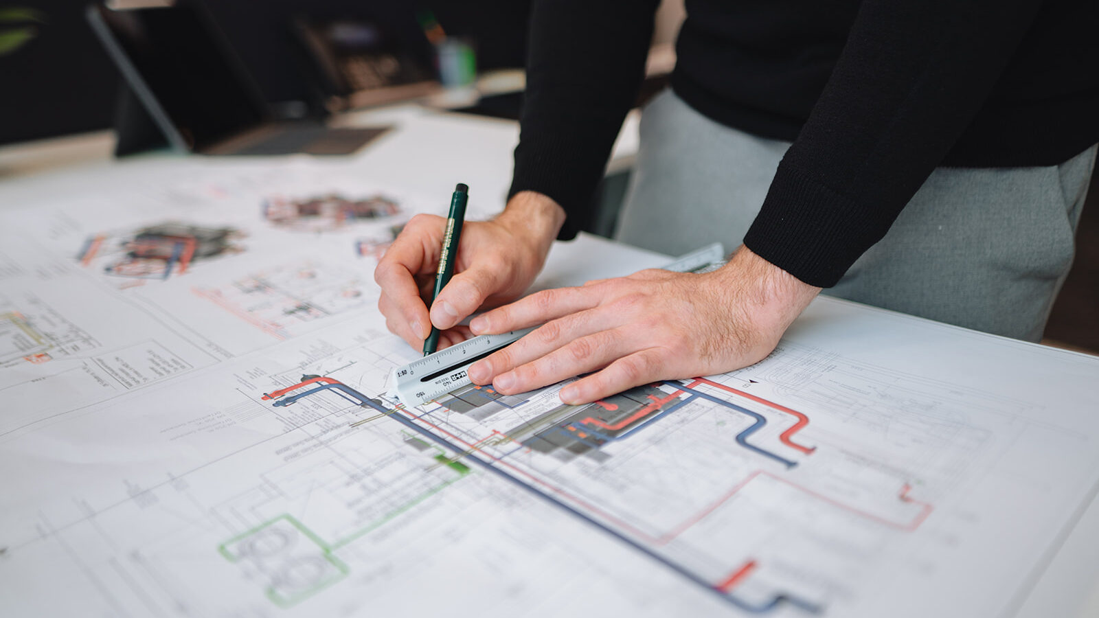 Zwei Hände ziehen mit einem Lineal eine Linie auf einer technischen Zeichnung.